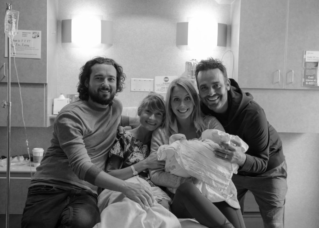 4 people looking at the camera smiling while holding a baby