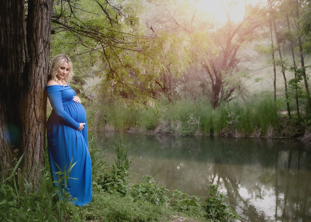 woman in blue dress standing by a tree by the river