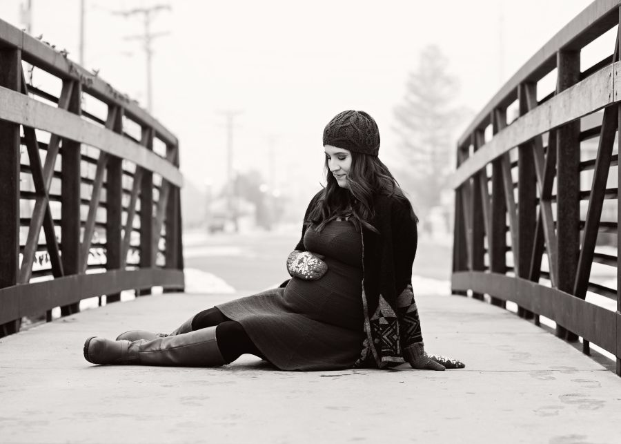 pregnant woman sitting down on a bridge while holding her belly with her hand